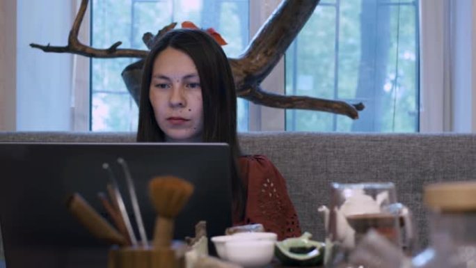 一个东方外表的美丽女孩坐在笔记本电脑的桌子旁，从事远程工作。在pondemic期间和之后在家进行远程