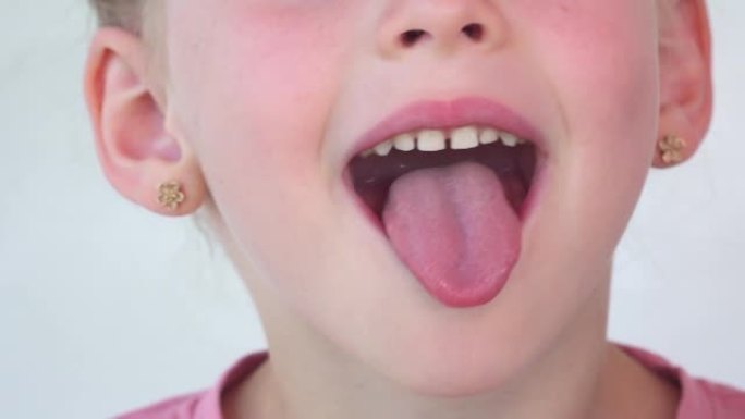 小女孩露出舌头，喉咙。孩子做体操。儿童训练肌肉进行言语治疗。白色背景上的快乐宝贝。文本的位置。张大嘴