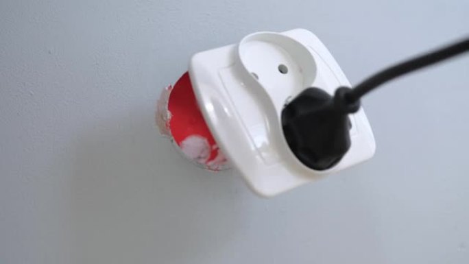 不小心粗心的高加索男性通过拉动电源线插头从墙上齐平安装的电气接线盒中撕下家用松动的电源插座