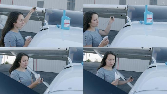 年轻的成年女性飞行员检查小型单引擎飞机的发动机油底壳上的量油尺