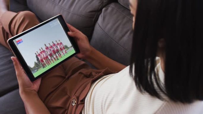 女性坐在家里的沙发上，用平板电脑看体育赛事