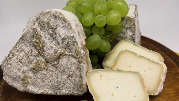 一盘各种发霉的山羊奶奶酪放在一块绿葡萄的木板上