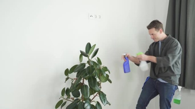 男人在家用喷雾瓶在室内植物花上喷水。家务和家庭概念