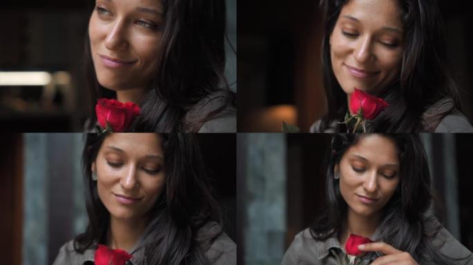 美丽的欧洲女孩长发黑发女人坐在沙发上，嗅着一朵红玫瑰向前看