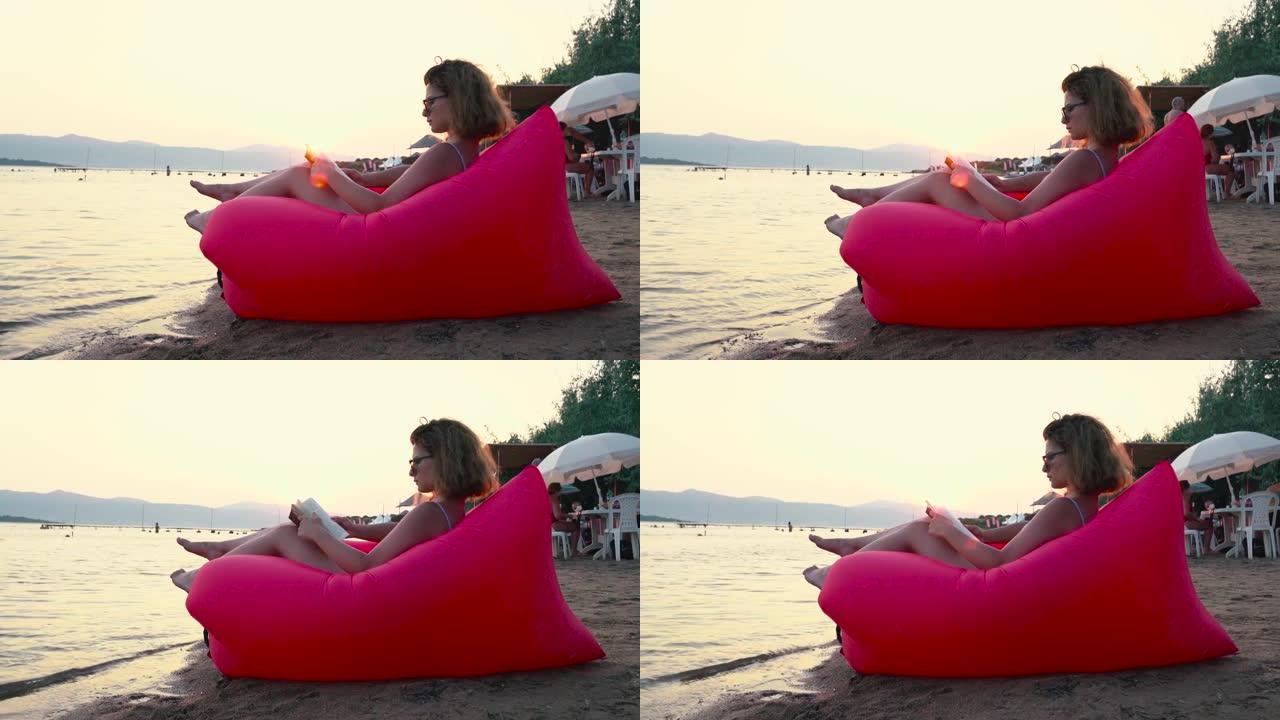 4k视频片段，一名年轻女子在红色贵妃椅的海滩上放松时看书