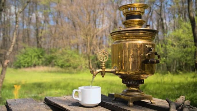 烟熏古董燃木茶炊。游客将茶炊中的水倒入杯子中。
