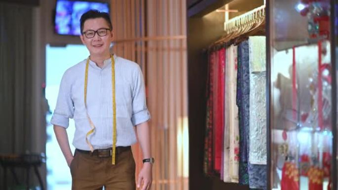 自信的男性传统中国婚纱时装设计师的肖像看着相机微笑着在他的设计工作室精品店