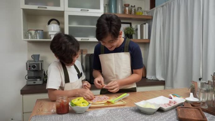 亚洲老大哥和小弟弟有一个有趣的活动来制作比萨饼，在周末一起添加火腿作为亚洲家庭有两个孩子的晚餐概念，
