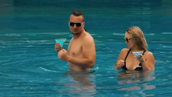 这对相爱的情侣在酒店室外的游泳池里拥抱亲吻，喝着蓝色的鸡尾酒。白种人男人和女人的肖像。