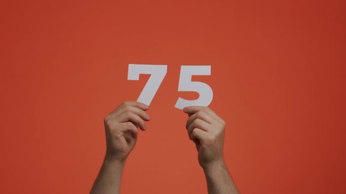 手中的七十五号。显示数字的人，75个由雕刻纸制成的数字，用于投票，数学学习或销售