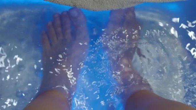 足部水疗中心。女人在水疗店的肥皂水机上赤脚按摩。妇女的脚在热水手持装置中进入洗脚盆。度假村水疗沙龙用