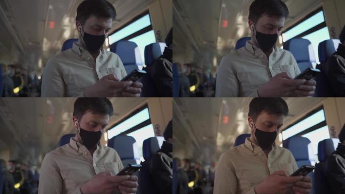 戴着口罩和耳机的男子乘客在乘火车安全旅行时使用电话在线观看视频和阅读新闻。公共交通工具中的病毒保护和