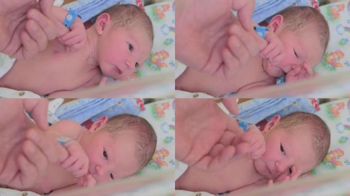 在妇产医院的婴儿床上，一个新生儿用手握着父亲的手指