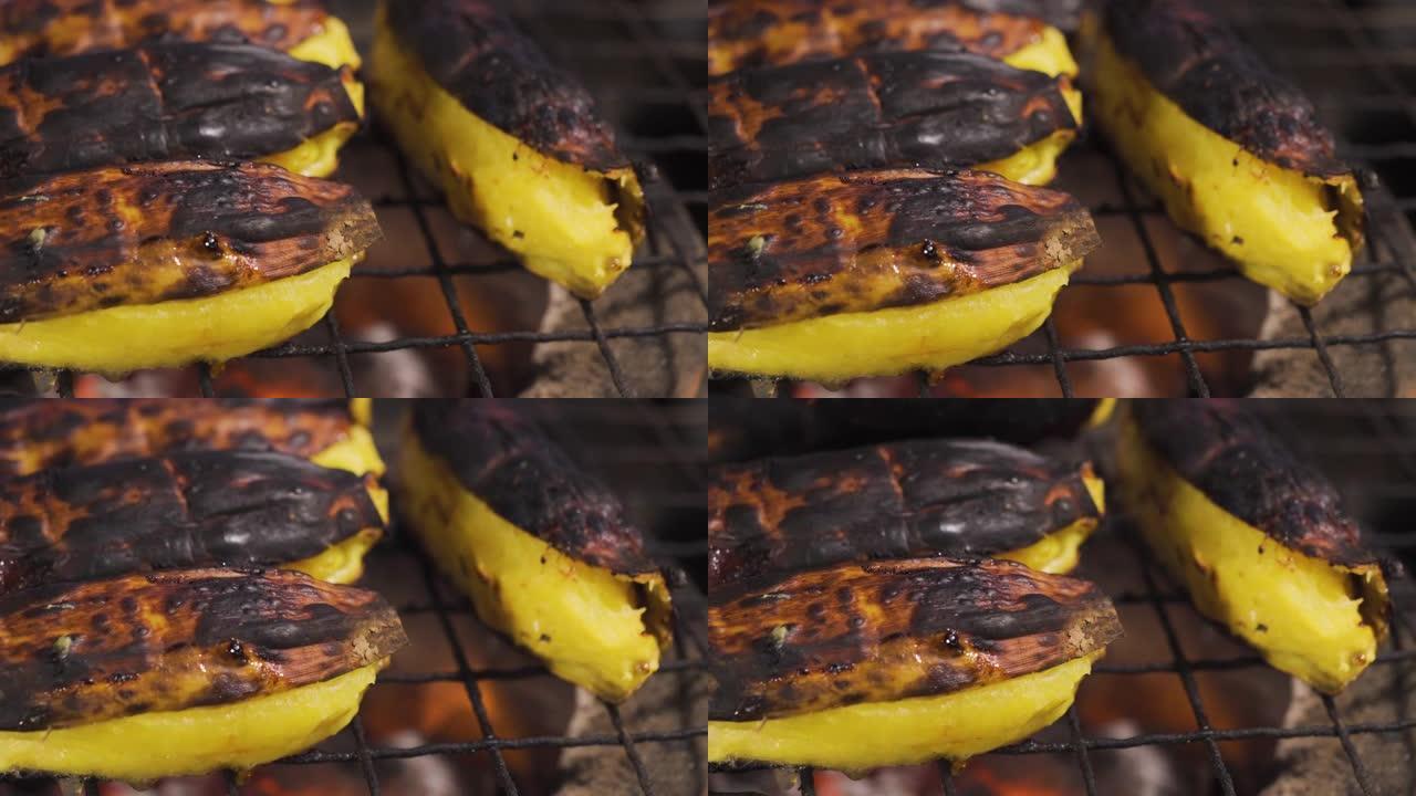 在传统的炭炉上烤香蕉，有人在后地面翻转烤香蕉。烧烤食物。泰国菜。热带地区的甜果甜点。