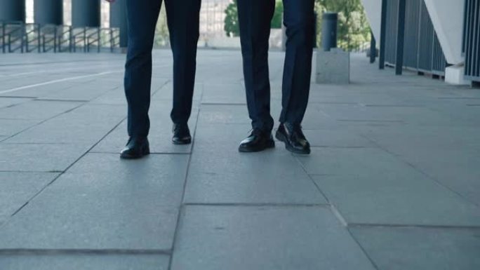 两个通勤上班的商人的前视脚。穿着皮鞋和正装的自信男人企业家沿着商业区的街道在户外行走