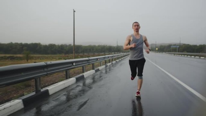 雷暴期间，运动员快速沿高速公路奔跑，正视图。运动男子在雨中在路上跑马拉松。短跑运动员做锻炼