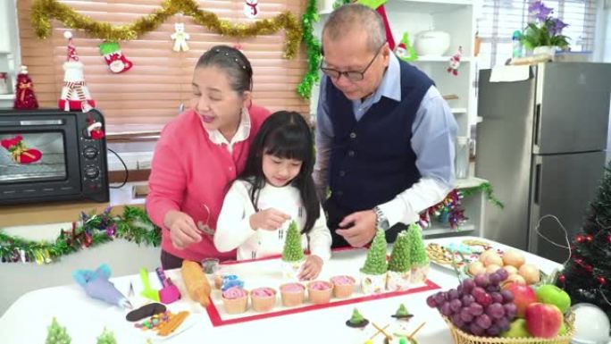 孙子，十几岁的女孩与祖父母，祖父，祖母一起学习准备圣诞树蛋糕。东南亚多代家庭的概念，在厨房里有一个孩