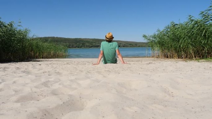 年轻人在平静的夏日里看着大自然，独自在沙岸湖后景和休闲旅行中休息。后视图盖伊徒步旅行者在生态徒步旅行