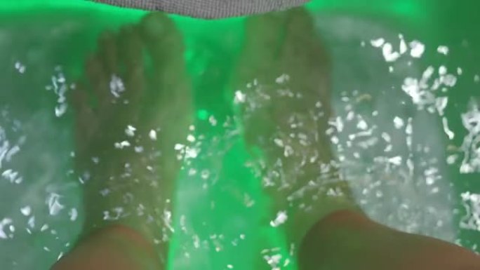 足部水疗中心。女人在水疗店的肥皂水机上赤脚按摩。妇女的脚在热水手持装置中进入洗脚盆。度假村水疗沙龙用