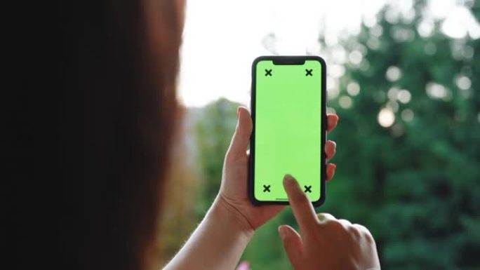 手持色度键绿屏智能手机的女性在不触摸或滑动的情况下观看内容的后视图。女孩用手机，浏览互联网，看内容