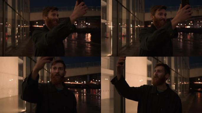 追踪年轻迷人的大胡子男人的镜头，晚上在城市街道上用手机在视频聊天中愉快地聊天