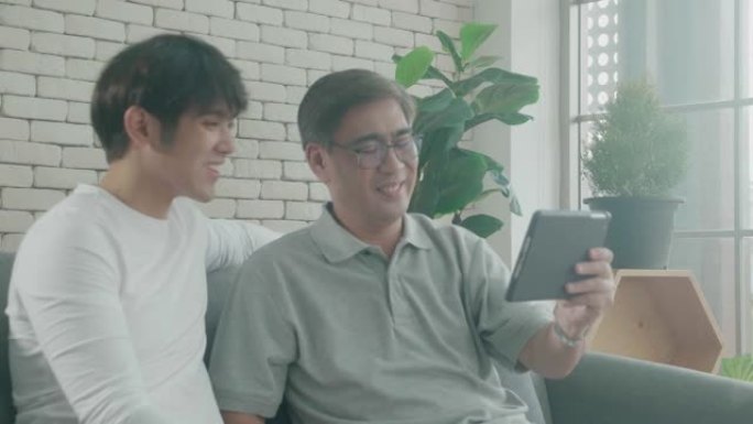 幸福的家庭，有父子坐在沙发上，在家里的平板电脑上与有趣的讨论，老人和年轻人看着平板电脑，一起聊天，交