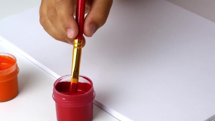 用油漆画画。孩子手里拿着画笔，蘸上红色颜料作画。4k视频特写。