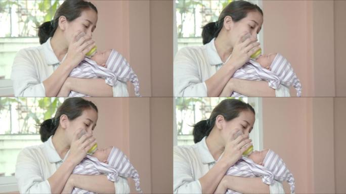 亚洲母亲抱着她的怀抱，用奶瓶给她可爱的小女孩喂奶。新生儿护理，父母身份，婴儿，生活，产妇，母亲，家庭
