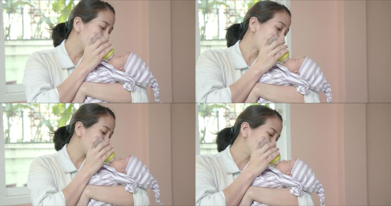 亚洲母亲抱着她的怀抱，用奶瓶给她可爱的小女孩喂奶。新生儿护理，父母身份，婴儿，生活，产妇，母亲，家庭