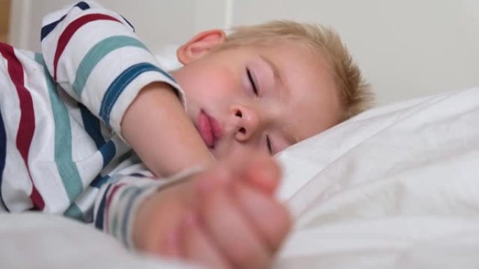 睡在床上的孩子。可爱的小孩甜蜜地睡在舒适的白色毯子上。2岁的孩子睡在婴儿床里。面对特写。白天睡觉时，