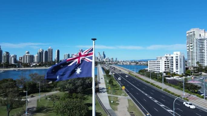 在繁忙的道路网络旁，通向高耸的城市天际线，在微风中挥舞着澳大利亚国旗的特写镜头。