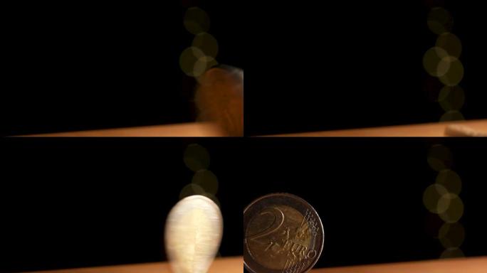 2欧元硬币旋转并落在黑暗背景下的桌子上