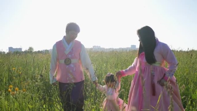 韩国家庭带着他们的女儿在日落时的草地上散步