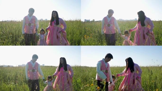 韩国家庭带着他们的女儿在日落时的草地上散步