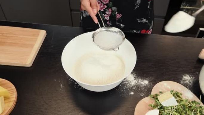 在准备比萨饼的面团时，用筛子筛面粉。女人用手筛面粉，为家庭烹饪传统的意大利披萨。烹饪过程