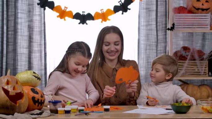 快乐的孩子和他们的母亲一起尝试南瓜和蝙蝠形状的剪纸面具。在家准备万圣节时一起玩乐。慢动作。特写