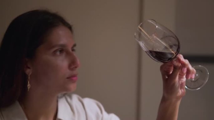 在餐厅或家中品尝葡萄酒，女人正在观看玻璃杯中的红酒