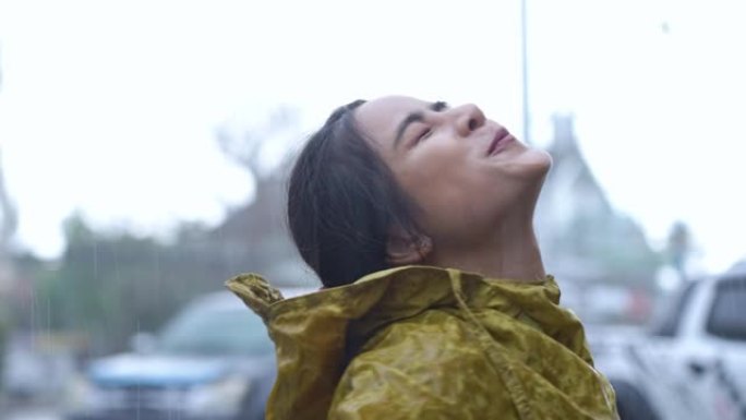 亚洲女孩脱下雨衣连帽衫享受落雨，站在路边，仰望天空享受雨滴对她的脸微笑，感觉新鲜，季节气候变化