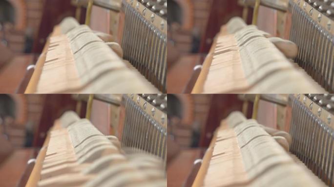 当一个人弹钢琴时，毛毡槌会主动敲击琴弦以产生声音或音乐，近距离观察，从内部看，背景模糊。立式钢琴内部