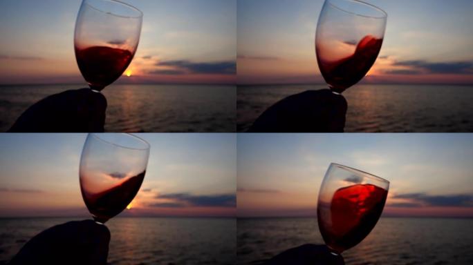 在海上日落的背景下，在玻璃杯中喝酒。慢动作。