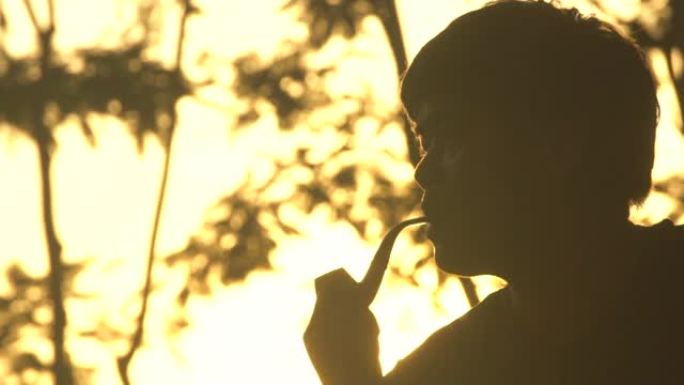年轻人坐在日落时抽烟斗。