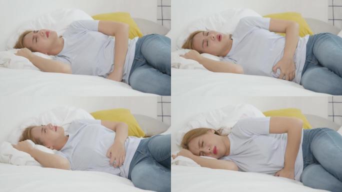 亚洲女人穿着上腹部腹痛，躺在床上，阳光直射，躺在白色卧室里。