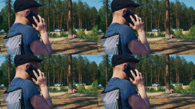 一个戴着帽子、留着胡子度假的年轻人正在用智能手机聊天。暑假在森林里治愈身体和灵魂。其他度假者也在安静