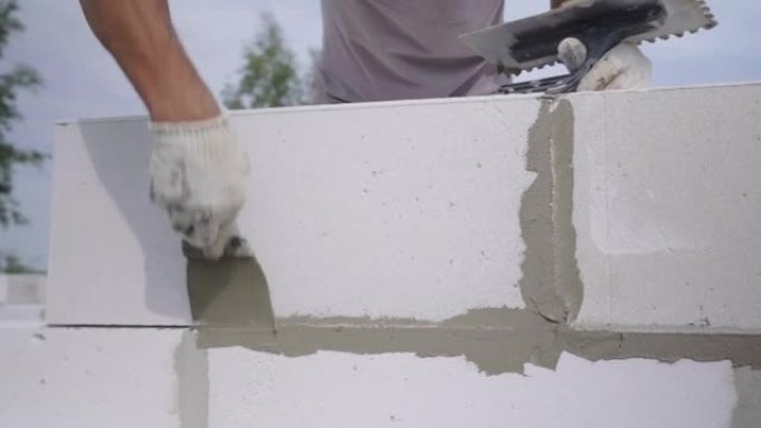 builder将粘合剂组合物或带有刮铲的溶液应用于墙壁结构。