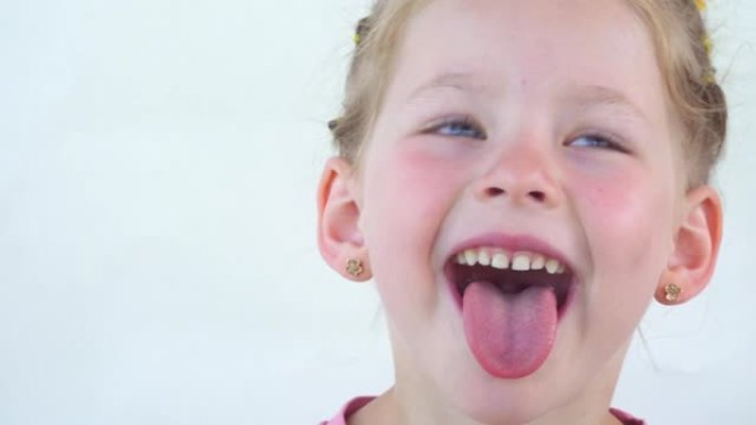 一个小女孩露出舌头，做体操锻炼杯子。训练舌头的肌肉来说话。言语治疗课。白底快乐的孩子。放置您的文字。