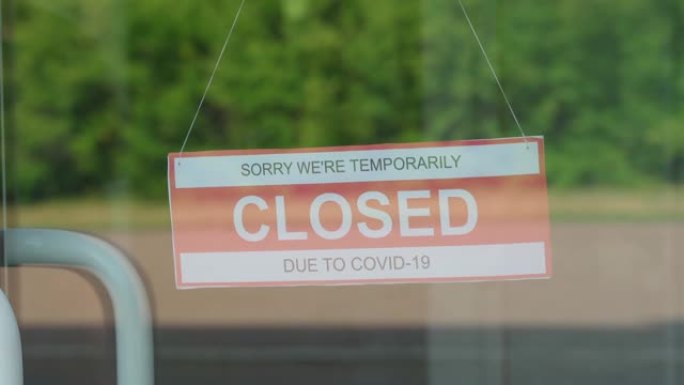 一名男子移除了一个在新型冠状病毒肺炎大流行期间被关闭的标志，该标志悬挂在透明的门上或店面里