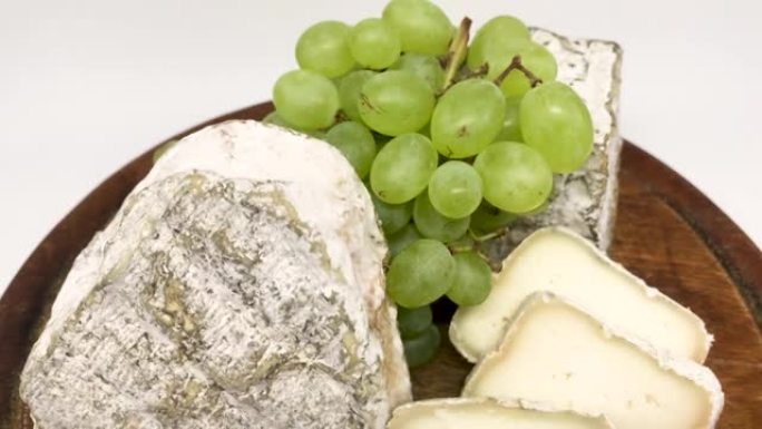 一盘各种发霉的山羊奶奶酪放在一块绿葡萄的木板上