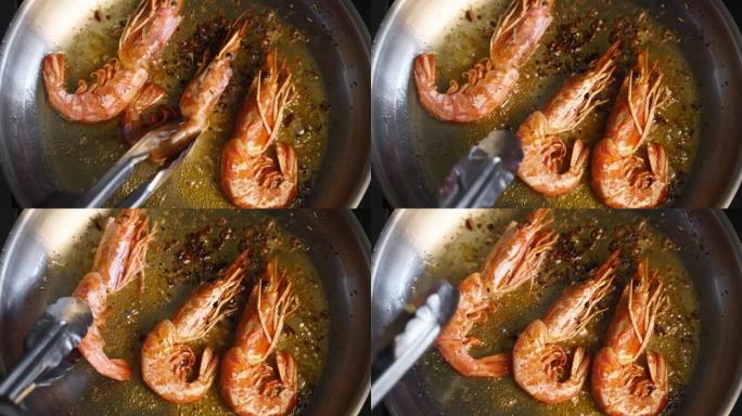 库克用镊子把虾放在烤架上。大虾在平底锅里煎炸的特写镜头。厨师在热锅上煎皇家虾。宏观海洋食品制备