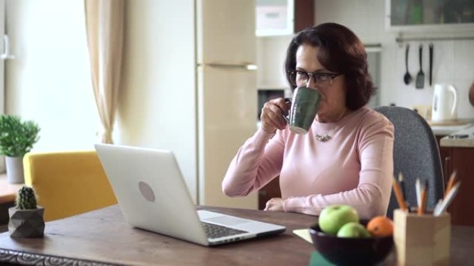 妇女在家庭办公室自学时使用笔记本电脑并在餐桌上喝咖啡