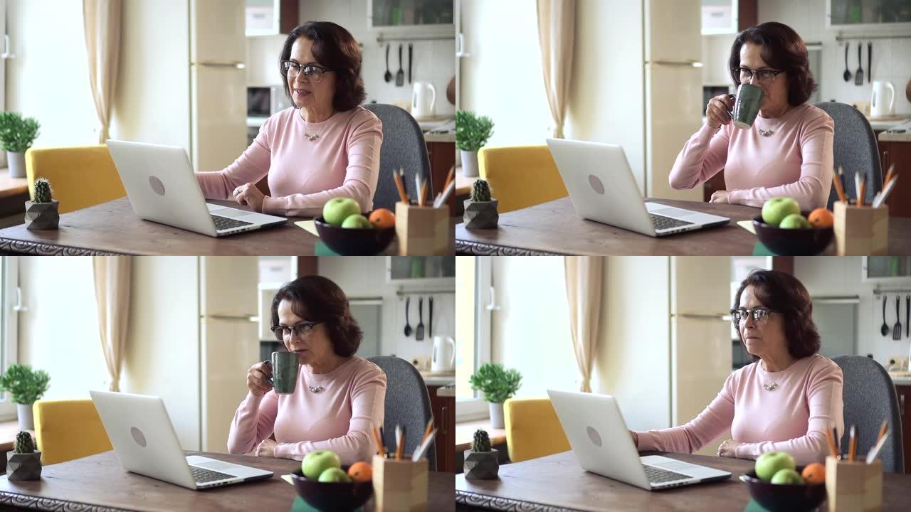 妇女在家庭办公室自学时使用笔记本电脑并在餐桌上喝咖啡